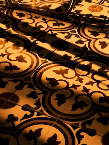 Detail of a golden-hued floor pattern illuminated by natural light through large windows.