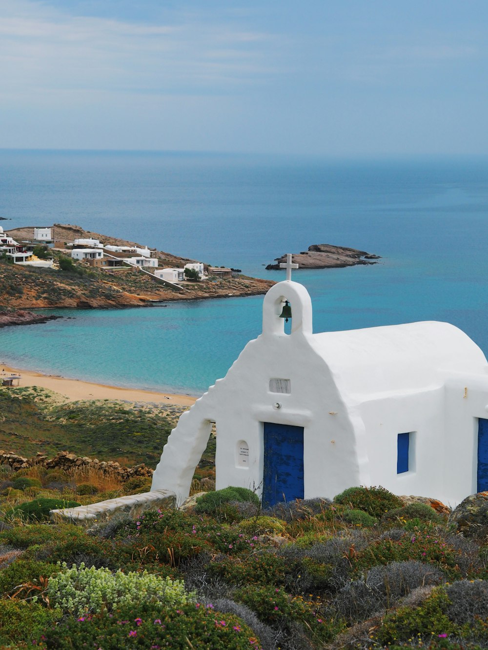 a white building with a blue door on a hill near the ocean