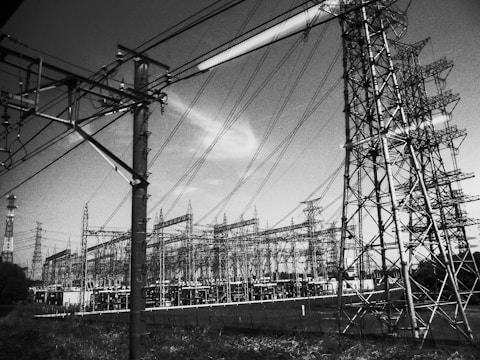 A complex structure of electricity pylons and wires extends across the landscape, with several large towers linked by numerous cables. The scene appears industrial and is dominated by the intricate metal frameworks of the towers and the crisscrossing wires.