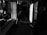 A person in a dimly lit, cluttered room seems to be engaged in cleaning or organizing. Debris and various items are scattered around, along with what appears to be a stroller on the right. The overall setting has a feeling of neglect or disarray.