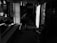 A person in a dimly lit, cluttered room seems to be engaged in cleaning or organizing. Debris and various items are scattered around, along with what appears to be a stroller on the right. The overall setting has a feeling of neglect or disarray.