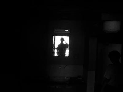 A shadowed silhouette of a negotiator observing intently in a dimly lit, navy-blue toned room.