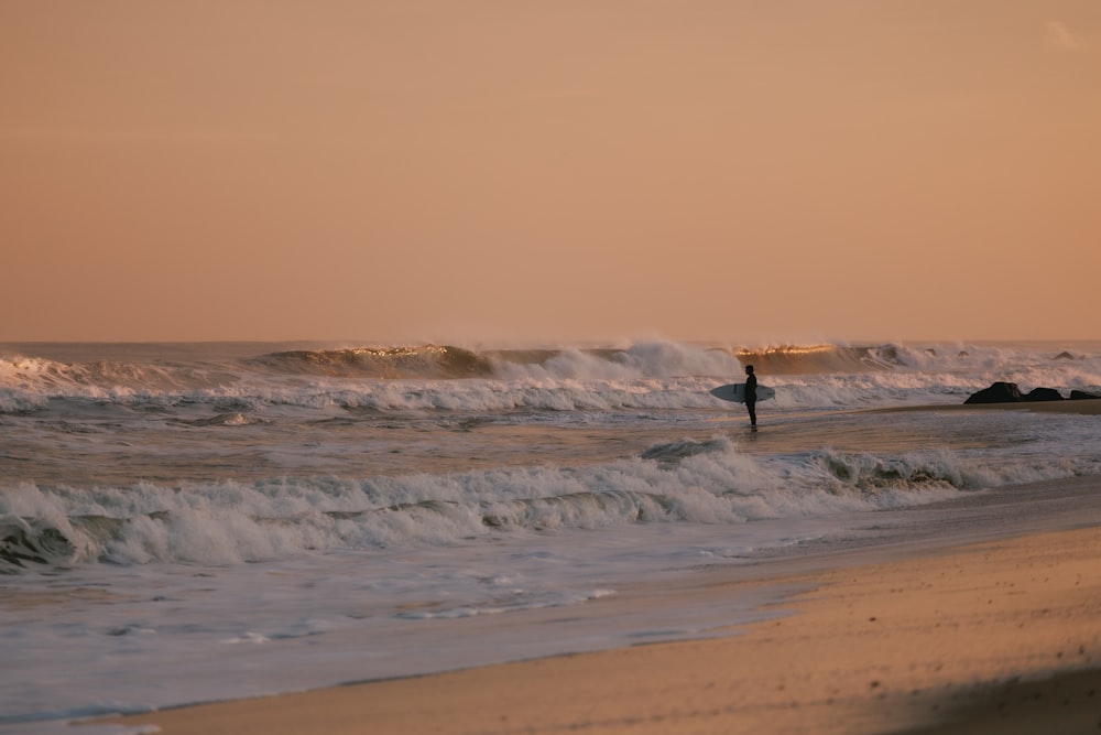 Una persona sosteniendo una tabla de surf caminando hacia el océano