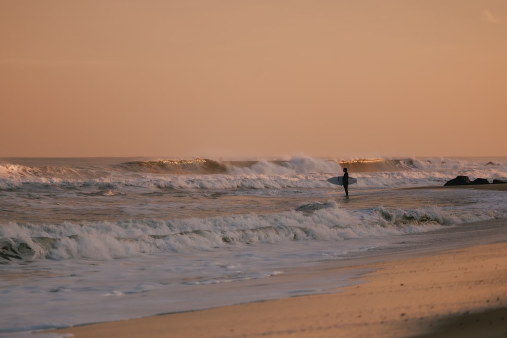 une personne tenant une planche de surf marchant dans l’océan