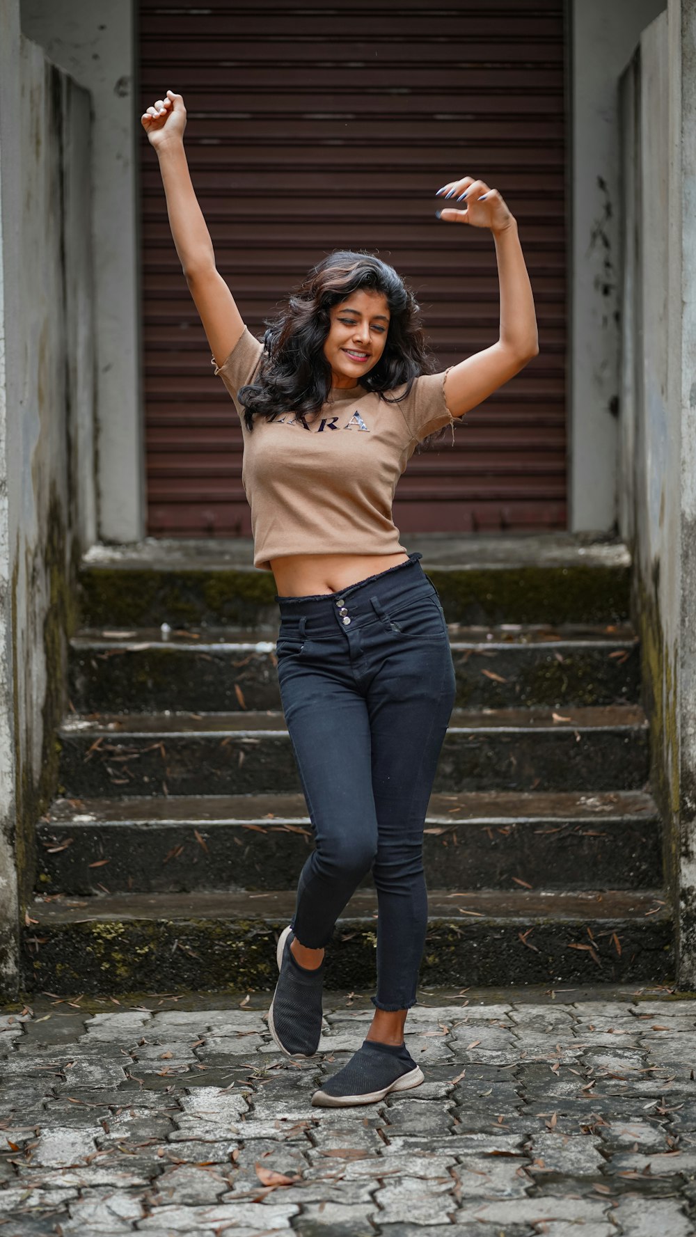 a woman in a tan shirt and jeans jumping in the air