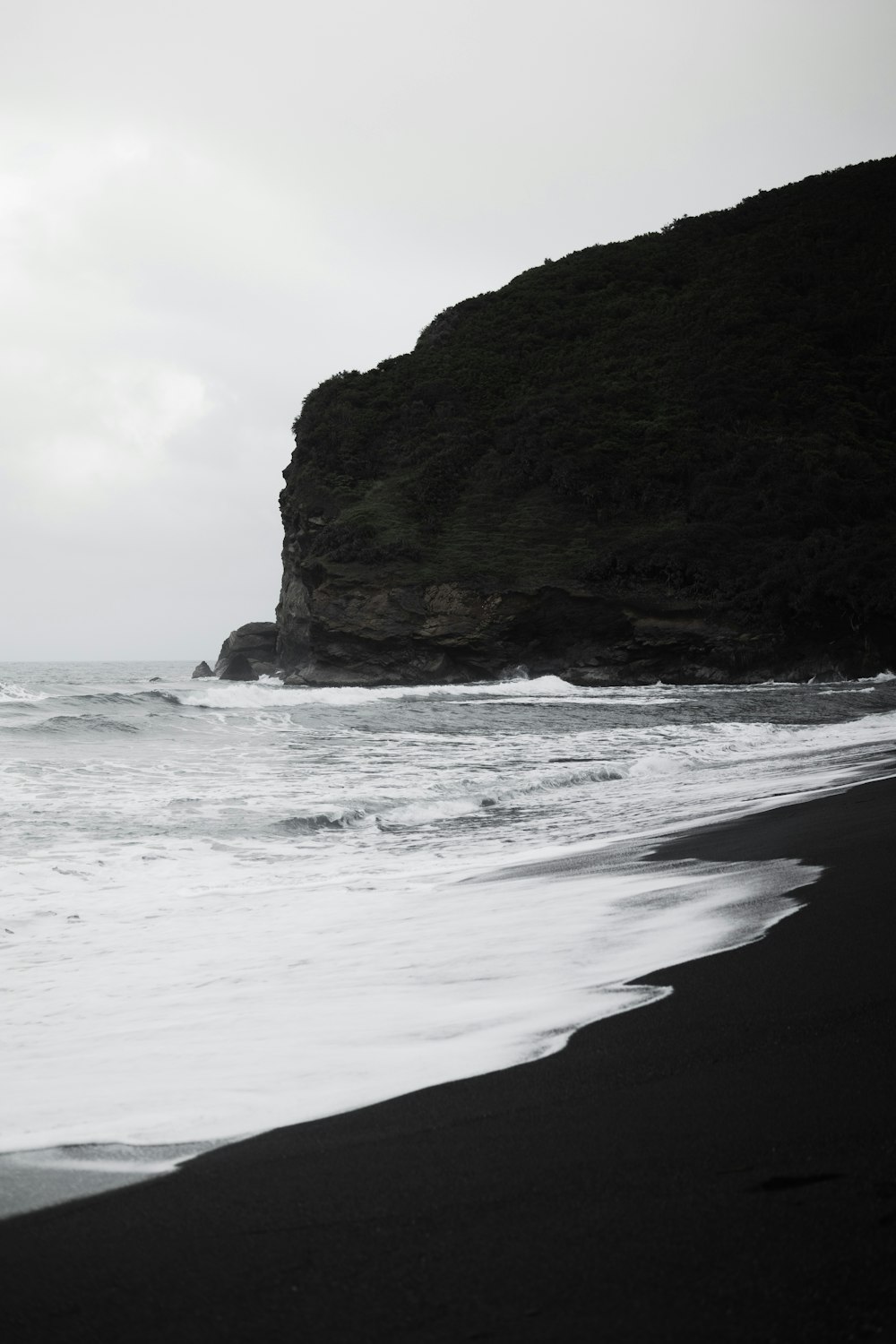 a black and white photo of a beach with a cliff in the background