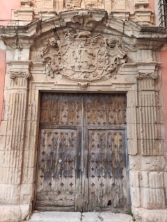 Close-up of an ornate family crest carved in aged wood above a heavy oak door.
