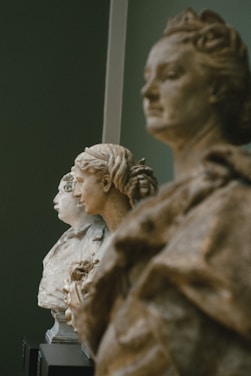 Three classical busts are lined up, showcasing intricate details in their hair and facial expressions. Each bust appears to represent a historical or mythological figure, positioned against a muted green background.