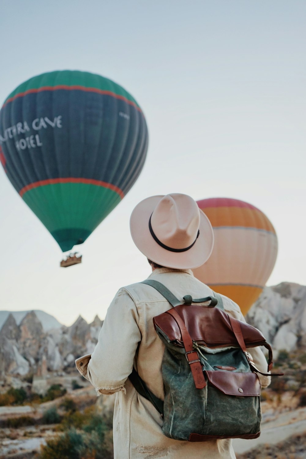 a man with a backpack and hat looking at hot air balloons