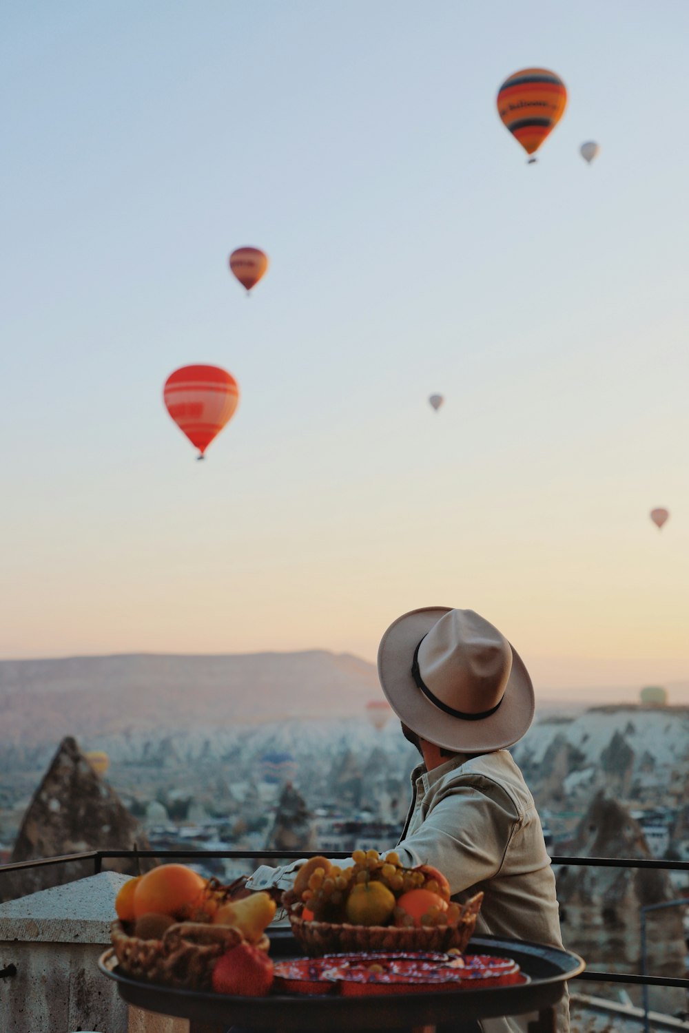 a person sitting at a table with fruit and hot air balloons in the sky