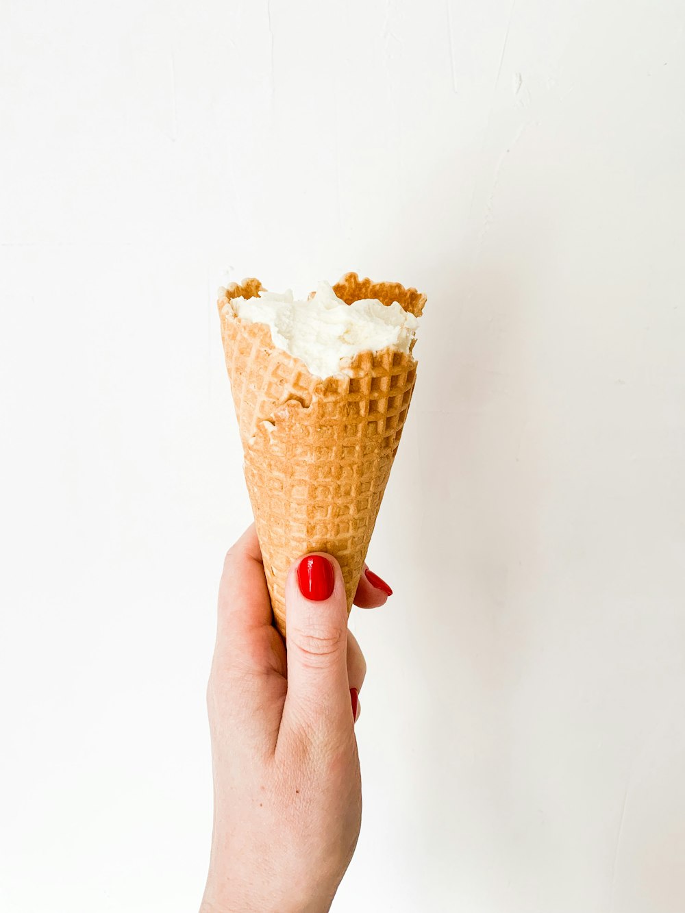 a hand holding a waffle cone with whipped cream