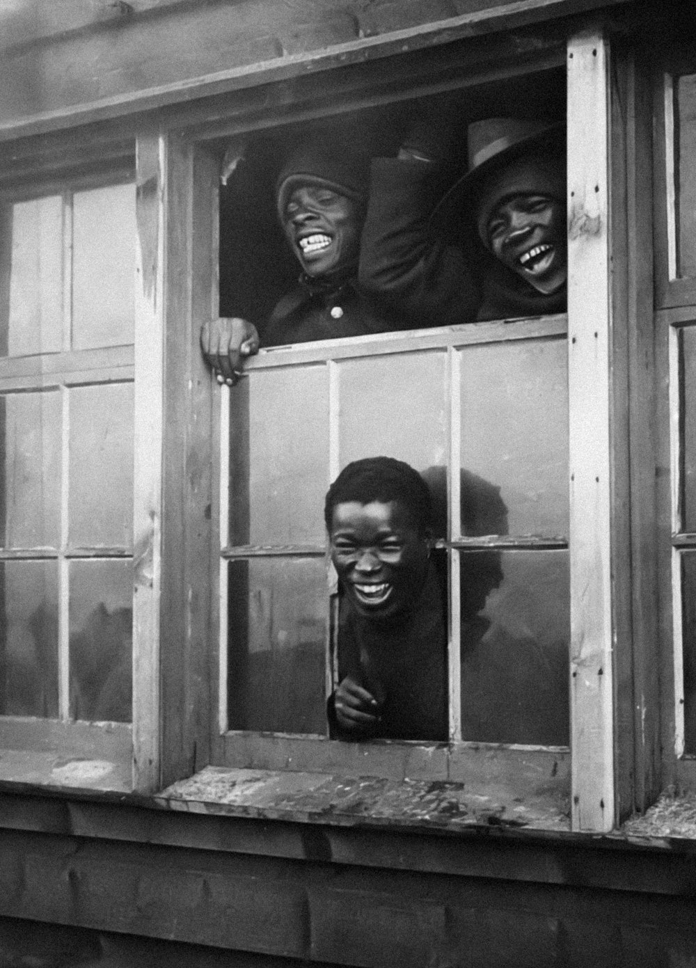 a black and white photo of three people sticking their heads out of a window