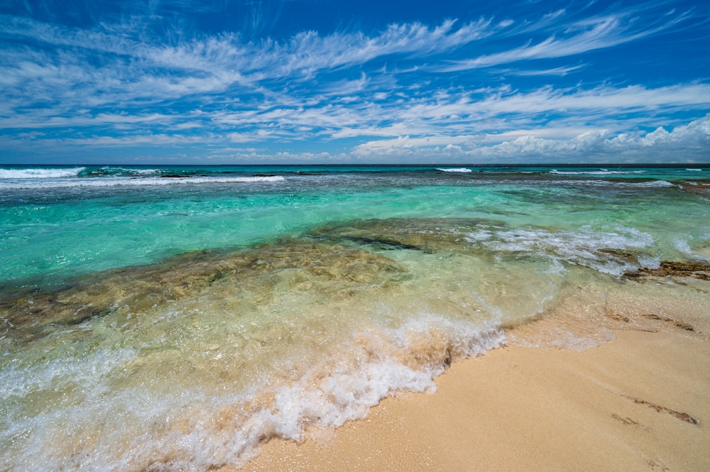 une plage de sable avec une eau bleue claire sous un ciel partiellement nuageux