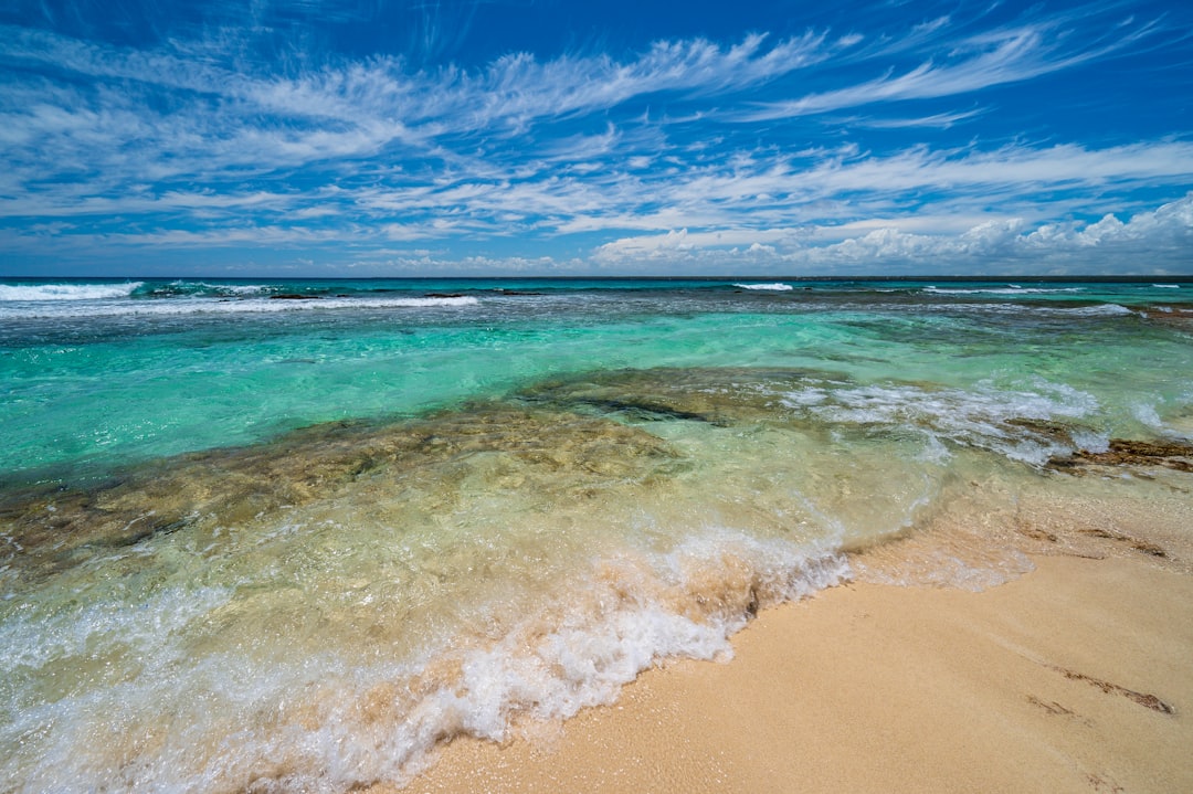 a sandy beach with clear blue water under a partly cloudy sky, Tropical paradise.