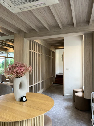A serene interior of a modern home featuring natural wood beams, linen drapes softly diffusing daylight, and a subtle butterfly sculpture on a stone shelf.