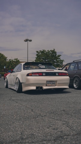 Side profile of a lowered street car with aggressive wide-body kit parked on an urban street at dusk.