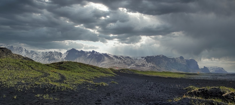 a dirt path leading to a mountain range under a cloudy sky