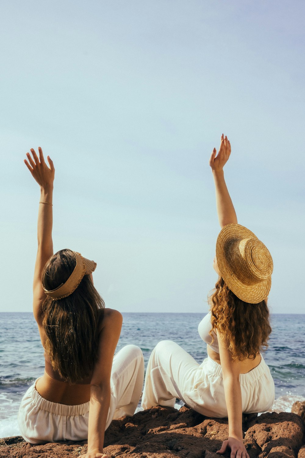 two women sitting on the beach with their arms in the air
