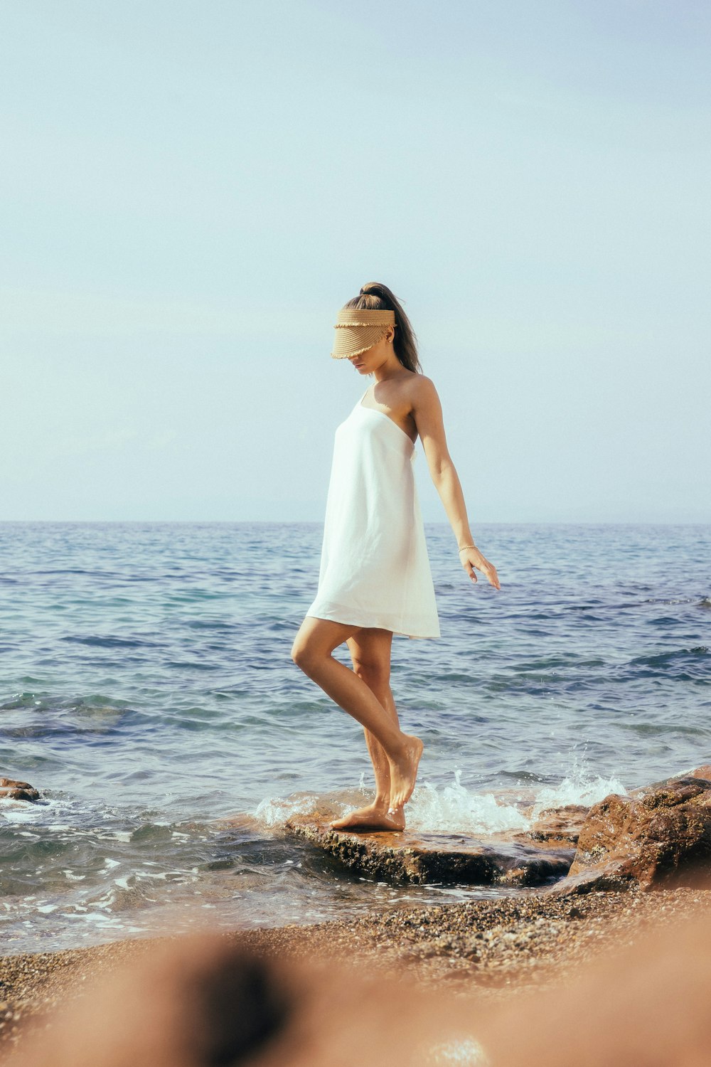 a woman in a white dress standing on a rock near the ocean