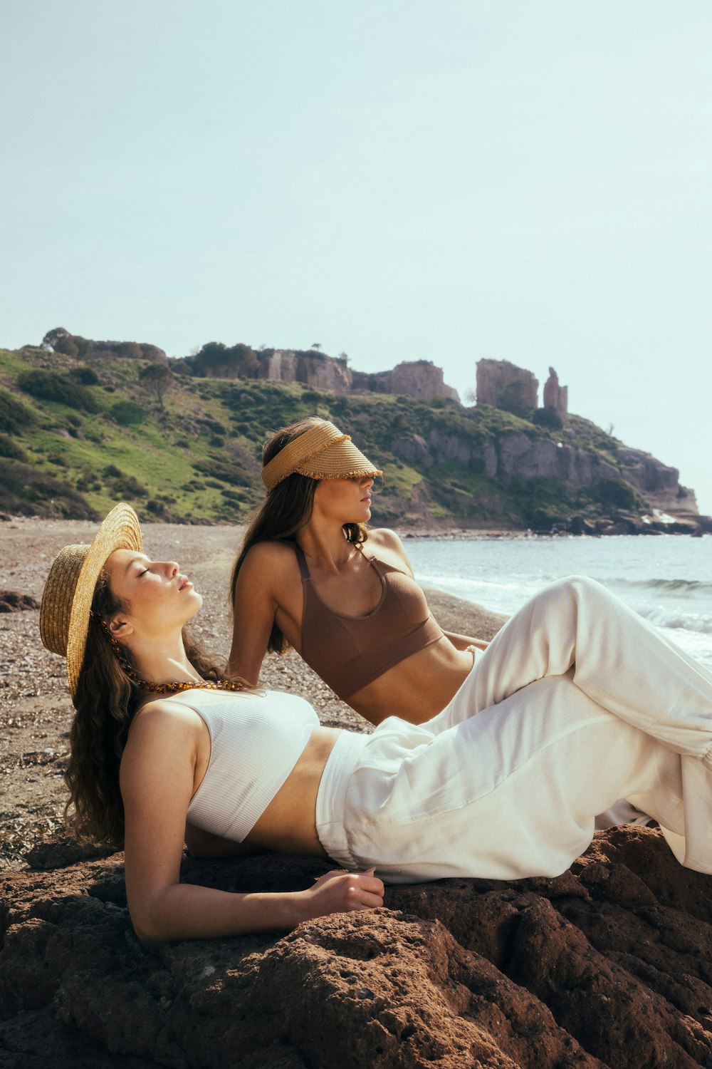 a couple of women laying on top of a rocky beach