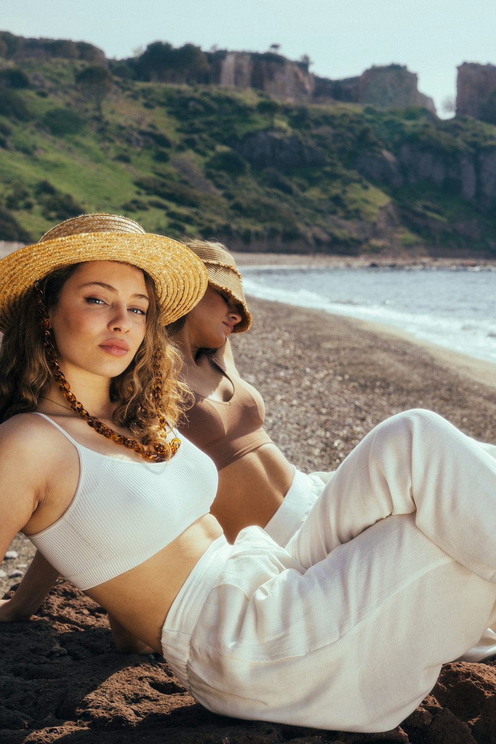 a woman sitting on the beach wearing a hat