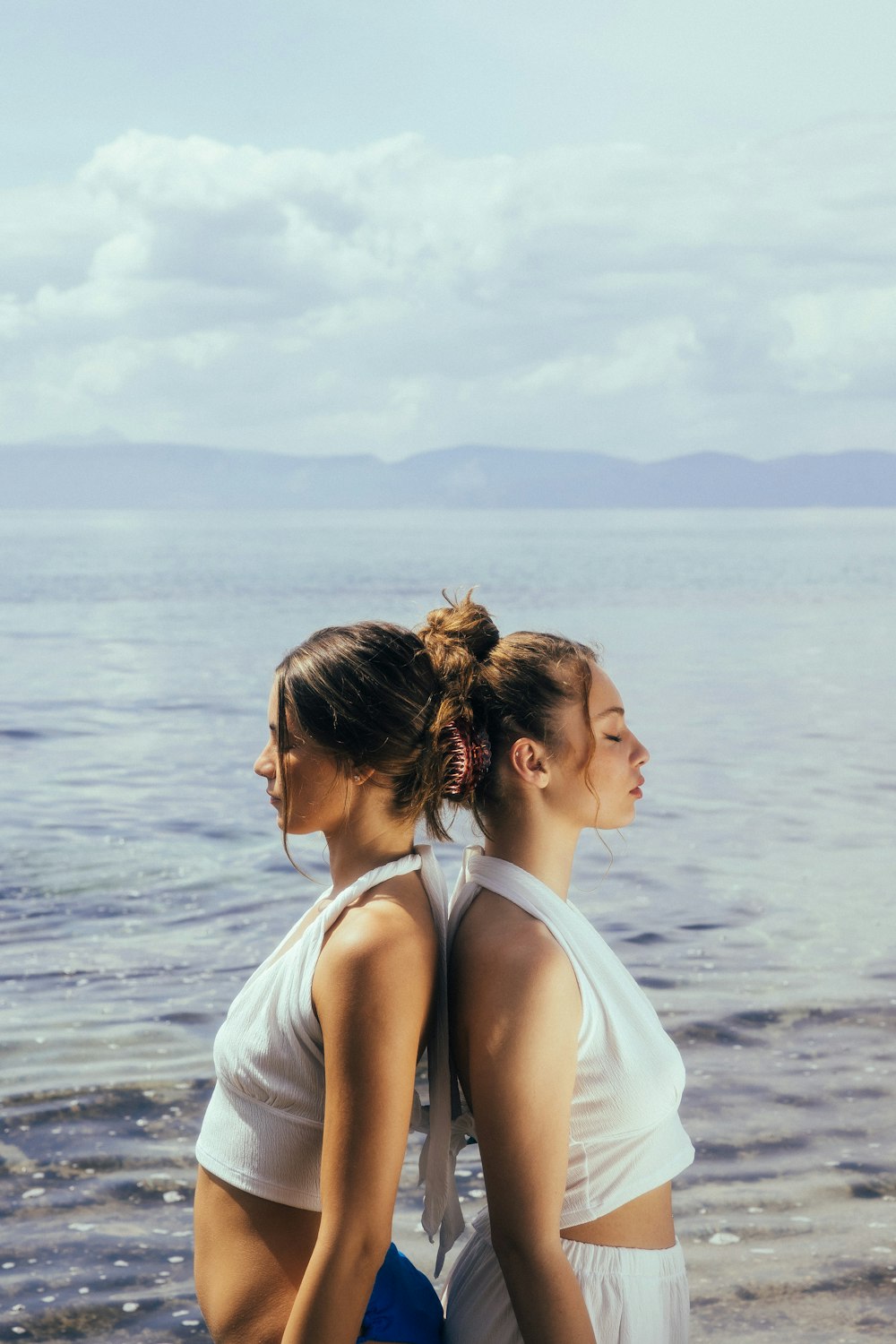 two women standing on a beach next to the ocean