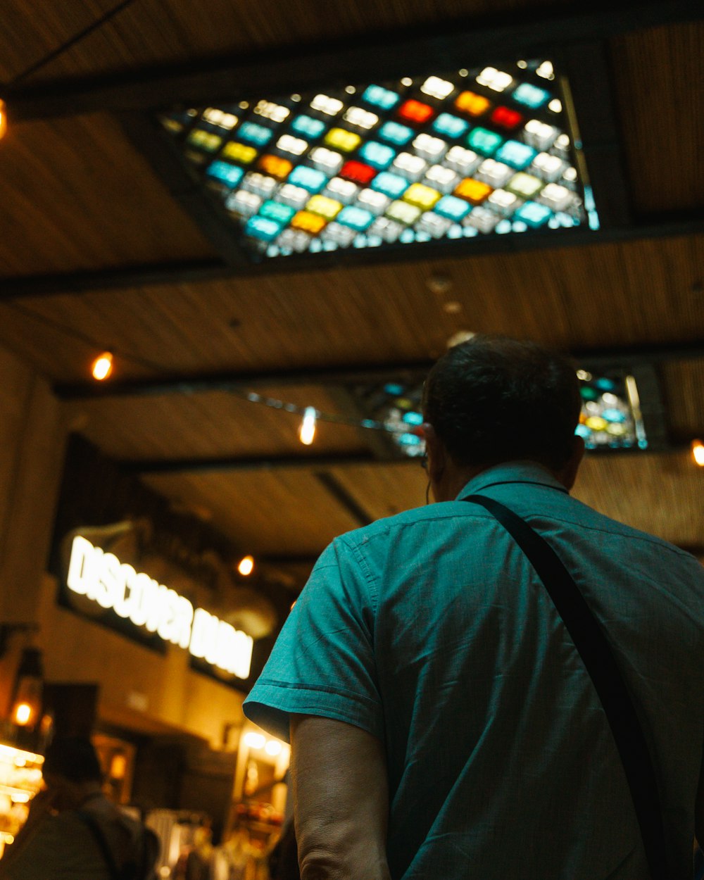 a man in a green shirt is looking up at a stained glass window
