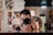 A person is taking a photo with a DSLR camera, capturing their reflection in a mirror. The background features a variety of colorful paintings and artwork, creating an artistic and vibrant atmosphere.
