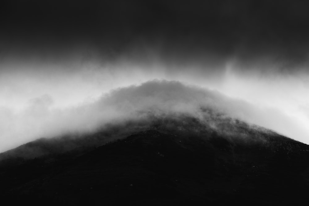 a black and white photo of a mountain covered in clouds