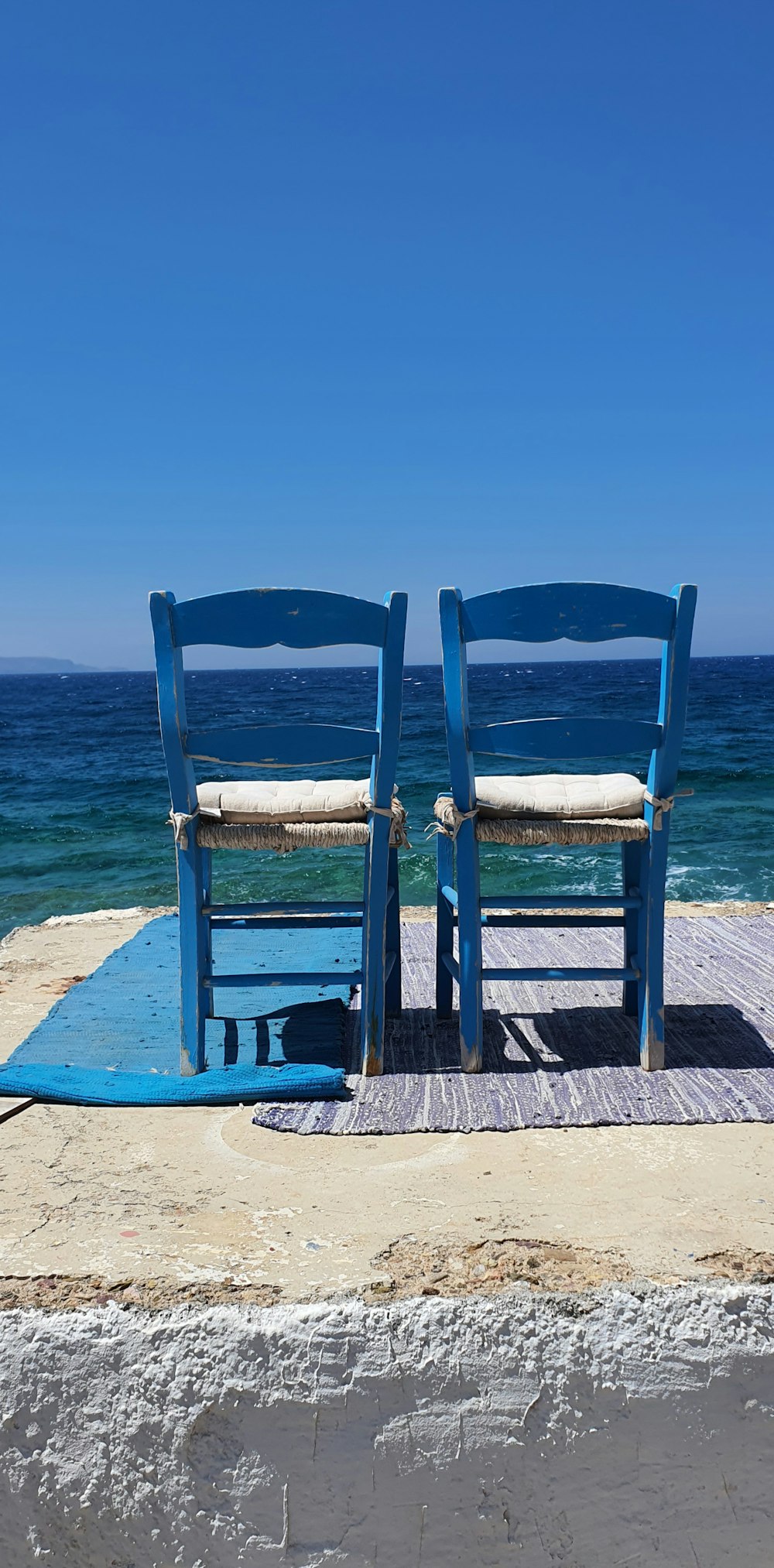 two blue chairs sitting on top of a sandy beach
