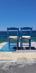 two blue chairs sitting on top of a sandy beach