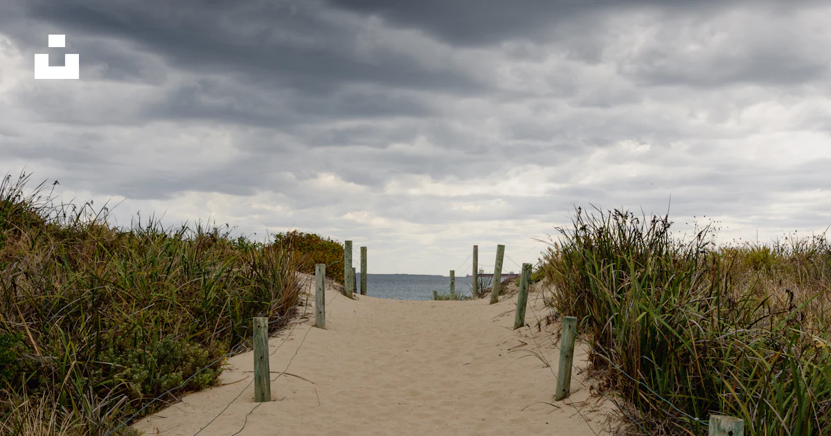 A sandy path leading to the ocean under a cloudy sky photo – Free Path ...
