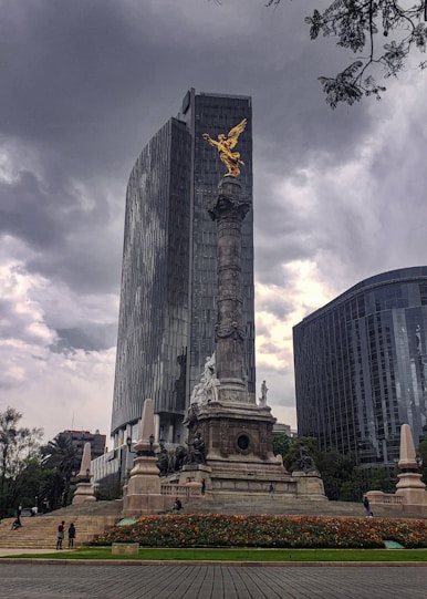 a statue in the middle of a park with tall buildings in the background
