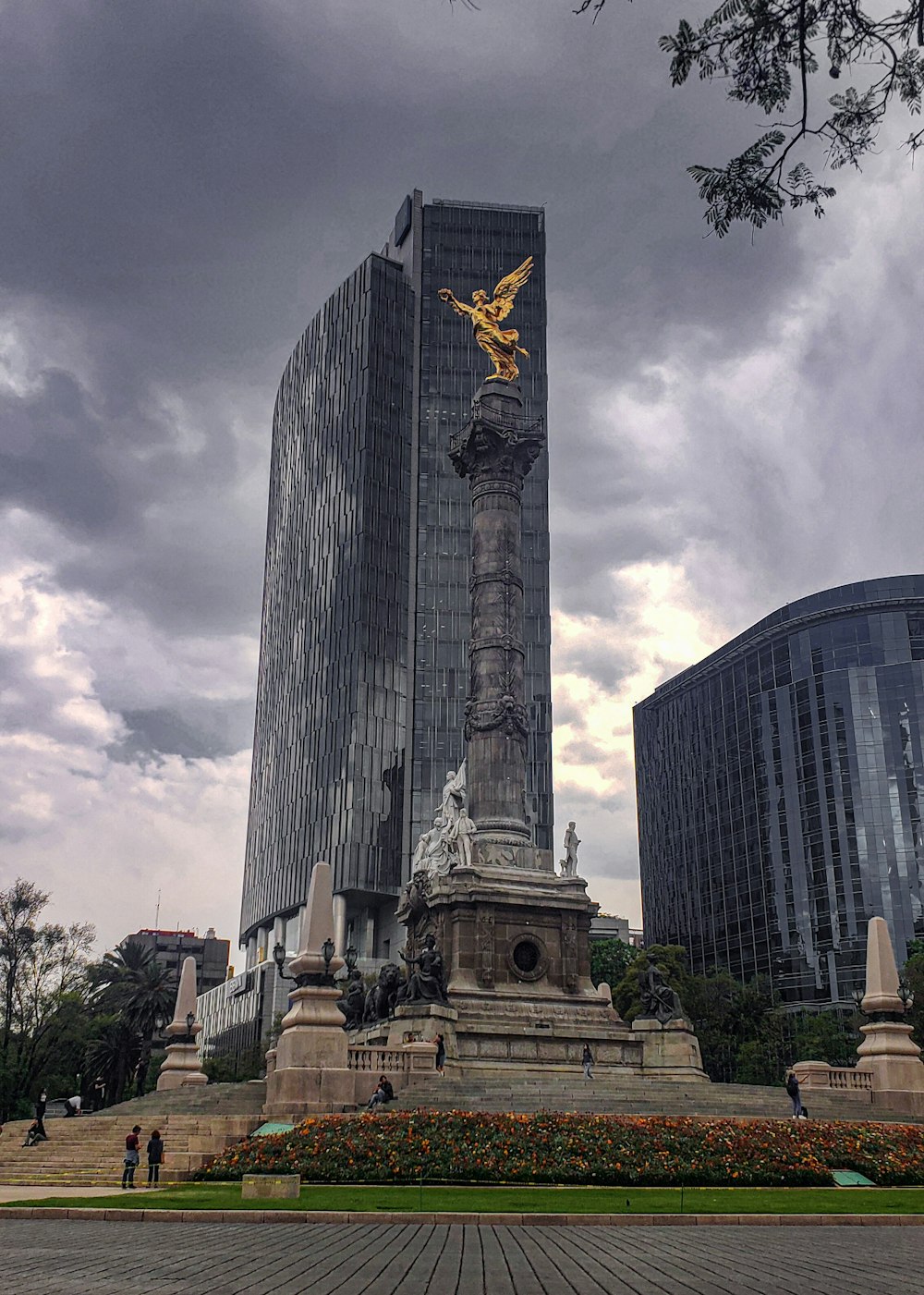 a statue in the middle of a park with tall buildings in the background