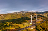 Expansive landscape of rolling hills with wind turbines silhouetted at dusk.