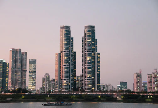 A sleek aerial view of a modern financial district at dusk, with illuminated skyscrapers reflecting in the river.