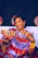 A joyful woman holding a colorful gift hamper with traditional Indian decorations in the background.