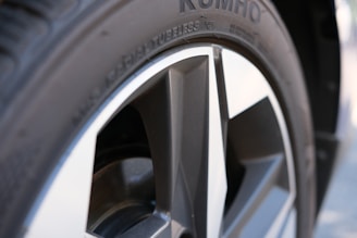 A close-up view of a car wheel with a five-spoke alloy rim and a tire. The tire's tread pattern and sidewall text are visible, including the brand name.