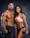 A muscular man and woman are posing confidently with dumbbells in their hands. The man is shirtless wearing black shorts, while the woman is wearing a pink sports bra and black shorts. Both display impressive physiques against a dark textured background.
