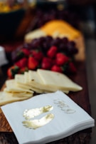 A close-up of a wooden board featuring sliced cheese, fresh strawberries, grapes, and decorative napkins with gold footprints printed on them.