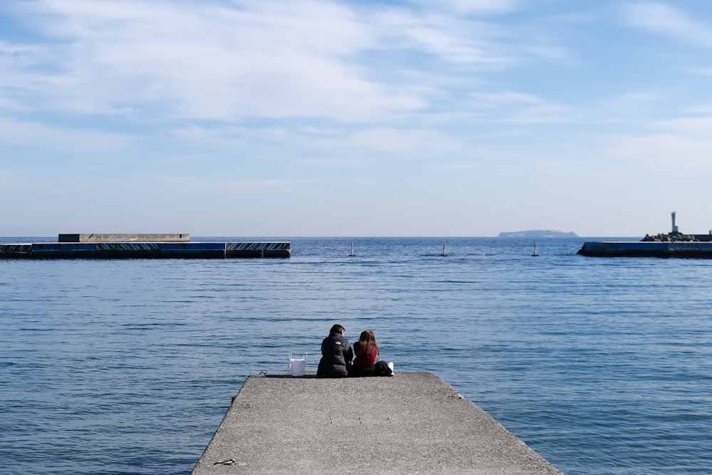 a couple of people sitting on top of a pier