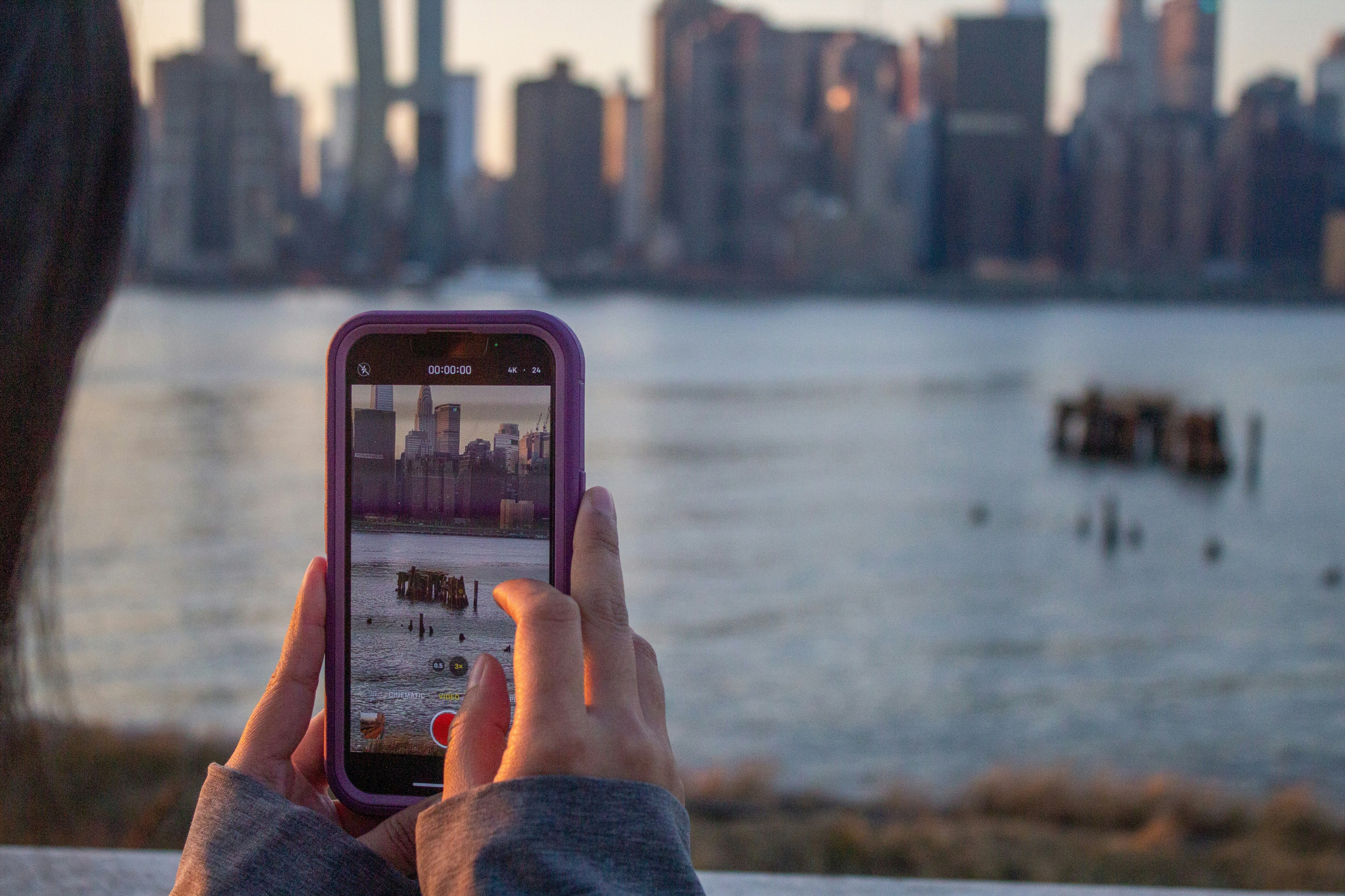 A person holding a smartphone showing a gold rate tracking app, with a blurred background of a city skyline, suggesting modern financial tracking.