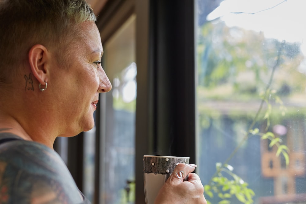 a woman holding a cup of coffee looking out a window