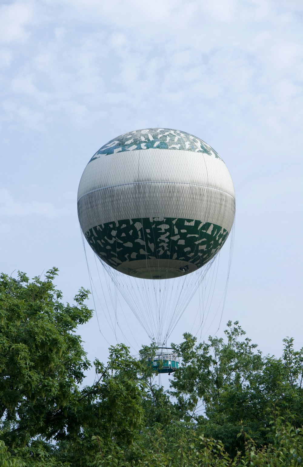 a large white and green balloon flying over trees