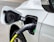 A close-up view of an electric vehicle being charged. The charging cable is securely attached to the port on the vehicle. The car is white, and the charging cable is predominantly black with a visible yellow section. There is a green indicator light on the charging port.