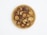 A wooden plate filled with dried fruit pieces, some with reddish edges and seeds visible in the center. The pieces have a wrinkled texture and varying shades of brown and red.