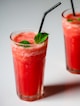 two glasses of watermelon drink with a black straw