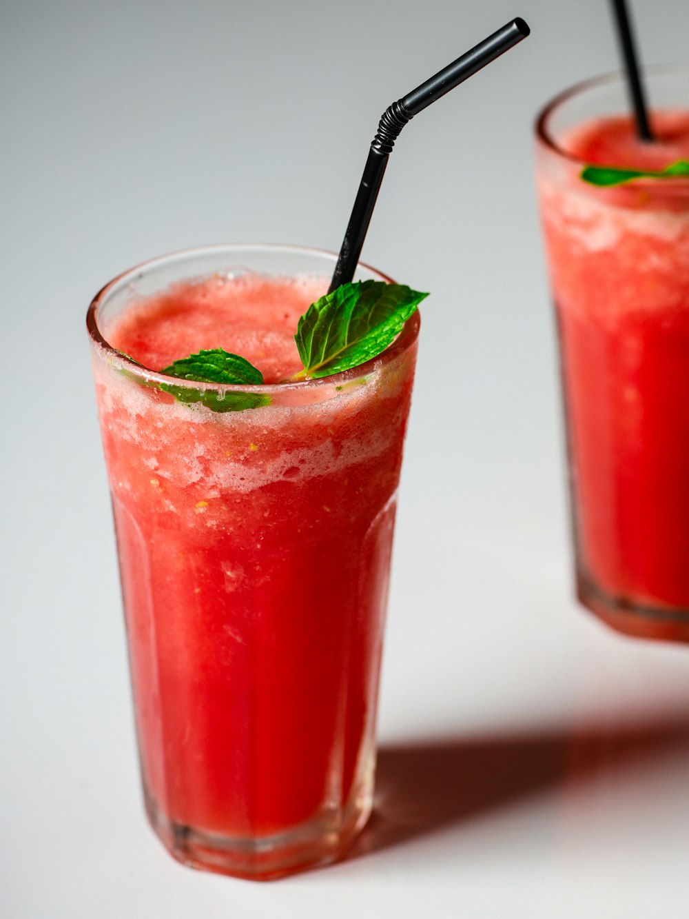two glasses of watermelon drink with a black straw