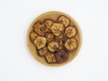 A wooden plate with dried fruit slices, featuring visible seeds and a slightly wrinkled texture. The fruit slices are arranged in a circular pattern on the plate.