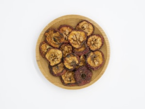 A wooden plate with dried fruit slices, featuring visible seeds and a slightly wrinkled texture. The fruit slices are arranged in a circular pattern on the plate.